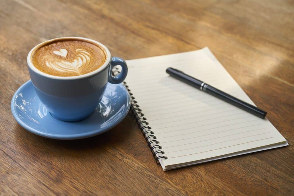 A coffee and a notepad with a pen on top of a table