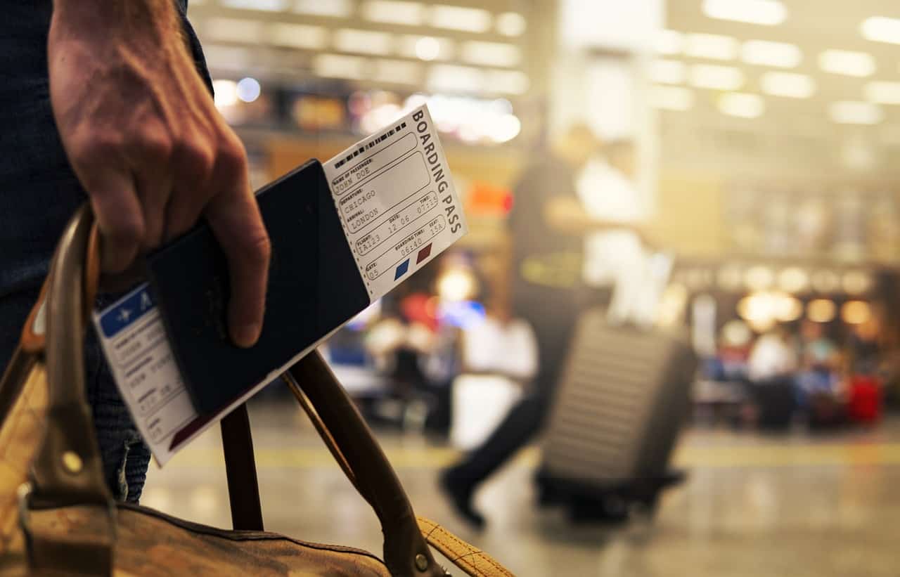 A person holds a U.S. passport at an airport with the airline ticket poking out at the top