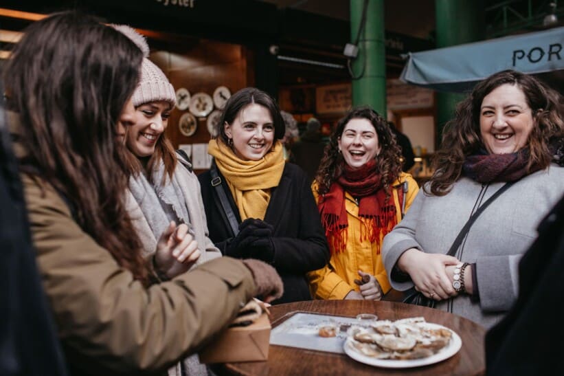 Five women enjoy an oyster standing at a tall table