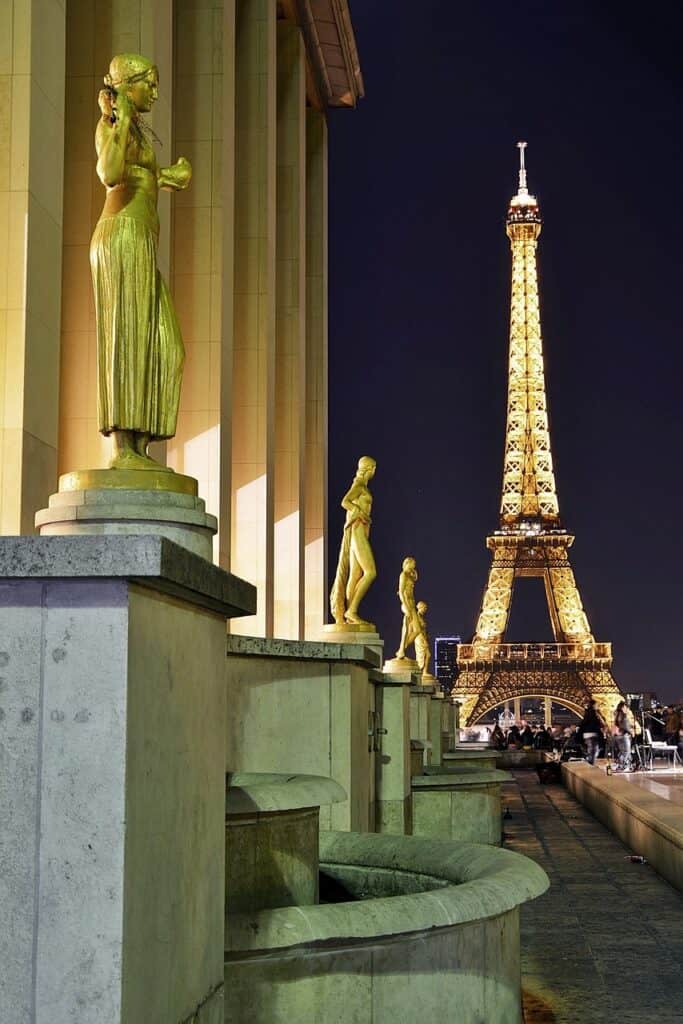 A view of the Eiffel Tower lit up at night with three gold statues nearby 