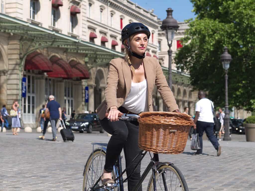 A woman wearing a black helmet rides a bike through Paris