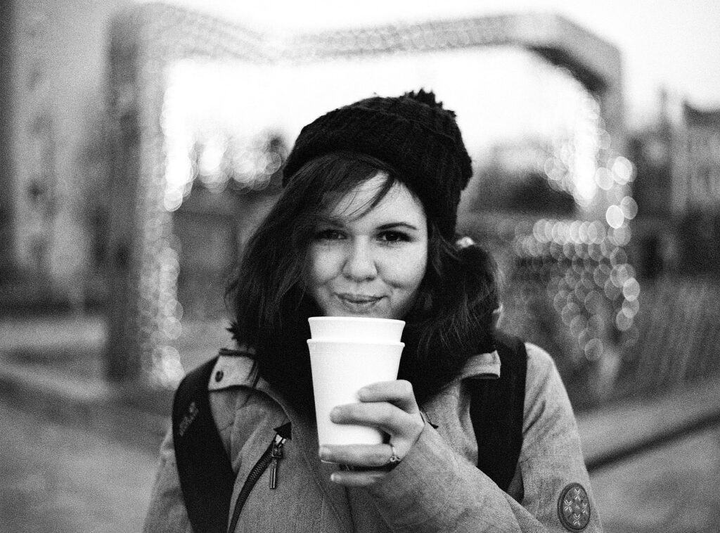 Black and white photo of a woman drinking hot beverage while wearing a hat