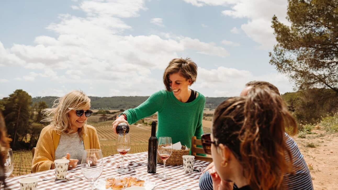 A woman pours red wine at a picnic table