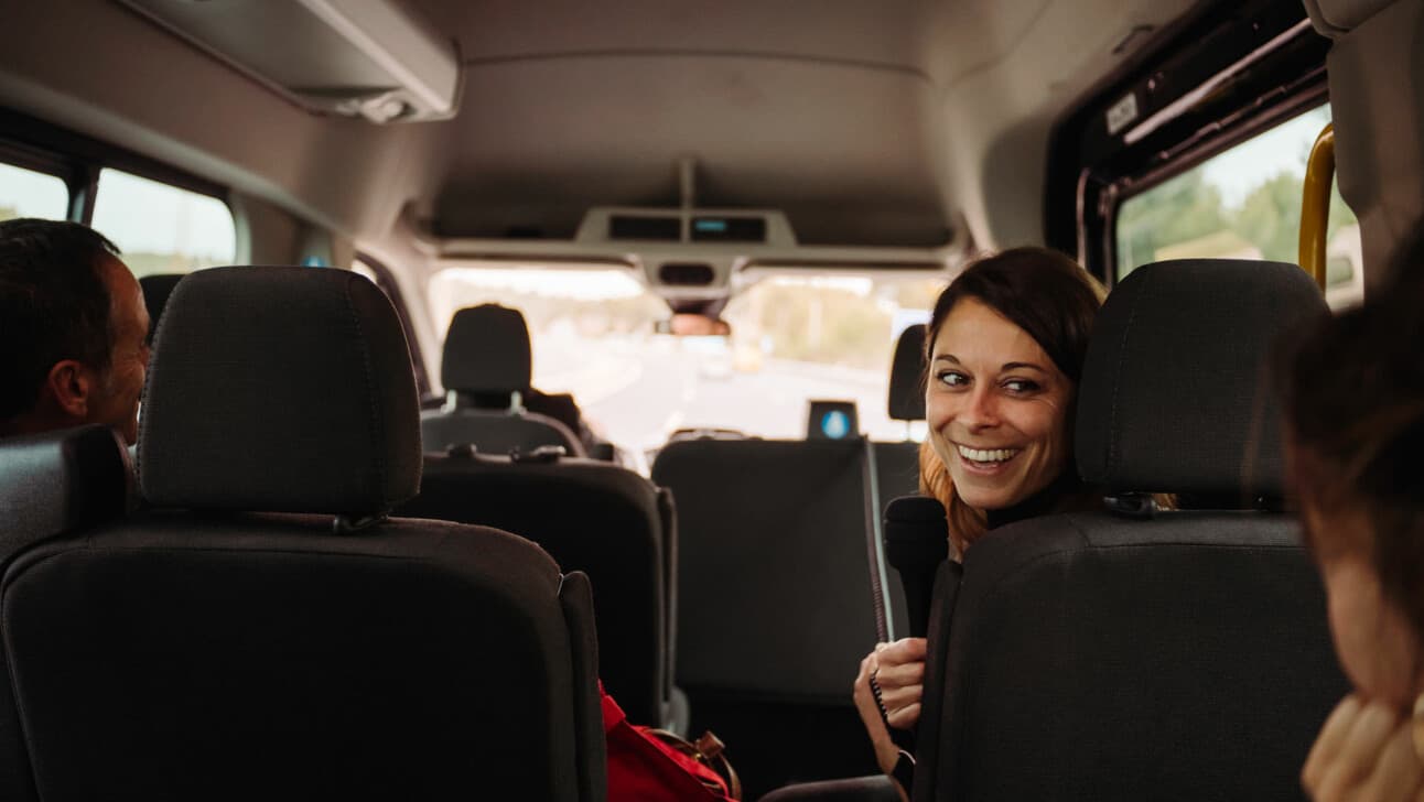 A smiling woman turns around inside a privately chauffeured van