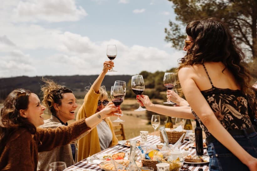 A group of woman cheers their red wine at a picnic table outside
