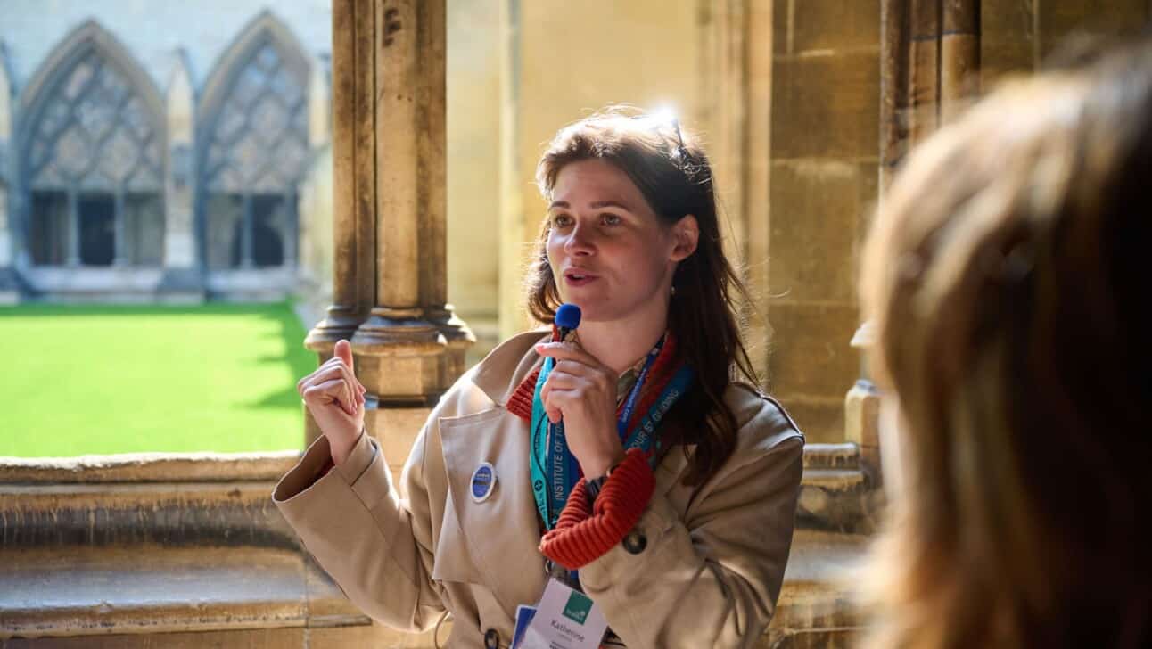 A blue badge guide leads a group through Westminster Abbey and stops to talk near a window