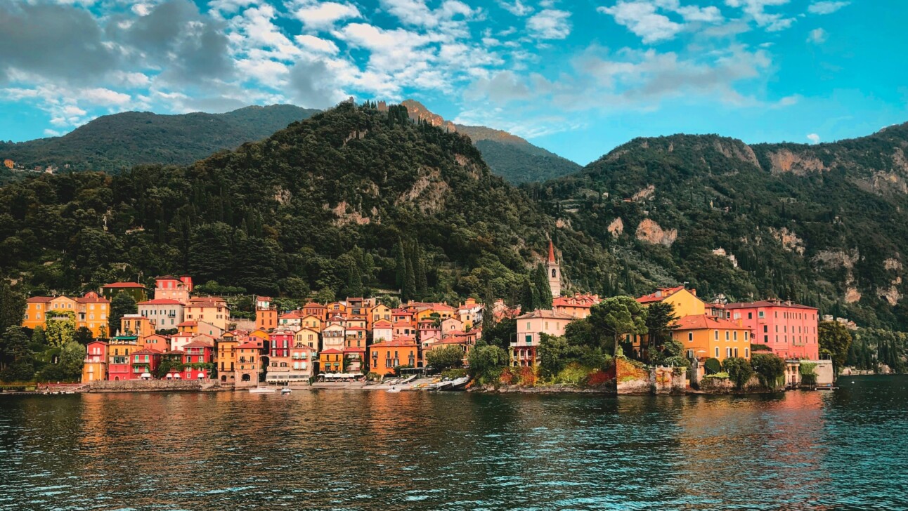 Yellow and orange houses along the edge of Lake Como with hills in the background