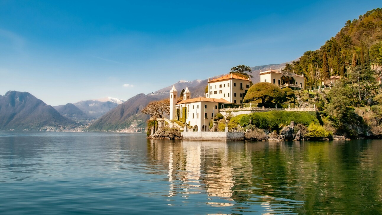 A beautiful white estate along the edge of Lake Como with mountains in the backgroun