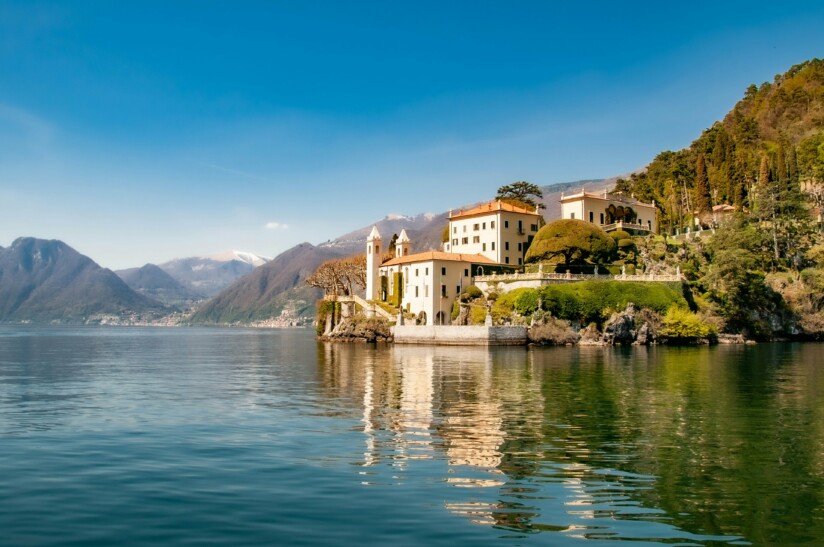 A beautiful white estate along the edge of Lake Como with mountains in the backgroun