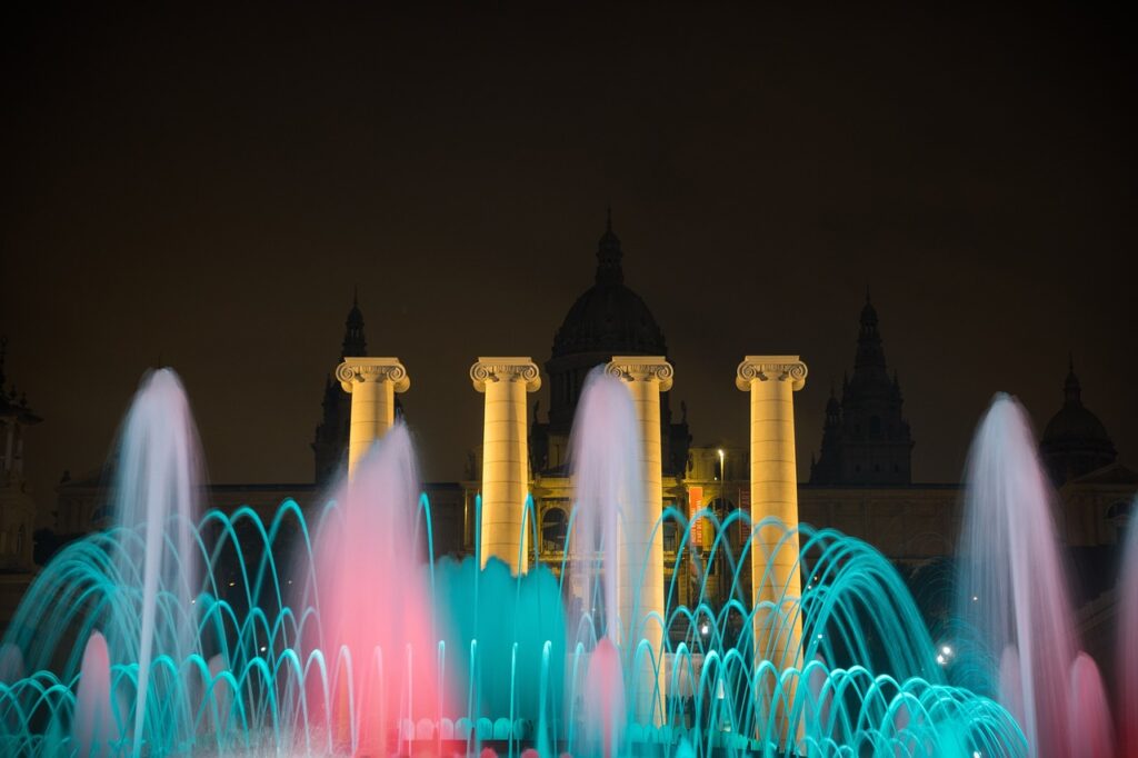 Barcelona's Magic Fountain lit up at night with blue and pink lights from the water
