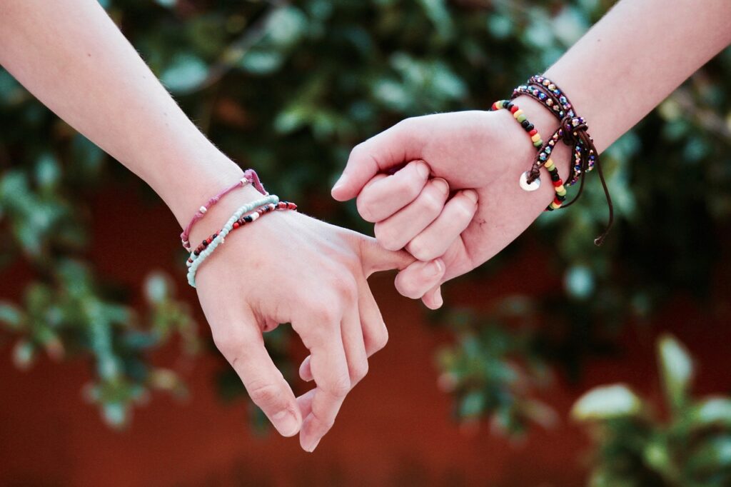 Two hands joined by pinkies and wearing multiple friendship bracelets